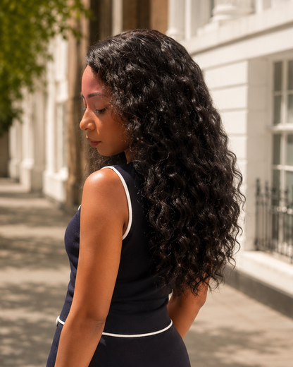 Woman in a black dress standing on a sunlit street with trees and buildings in the background