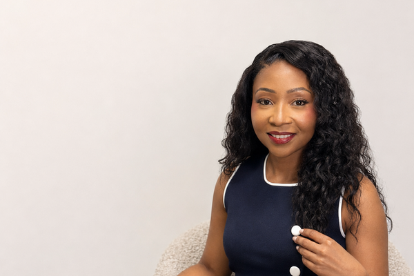 Woman with long, wavy hair wearing a navy blue dress with white buttons on a light background