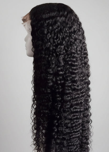 Black curly wig on a mannequin head against a white background - The Hair Source