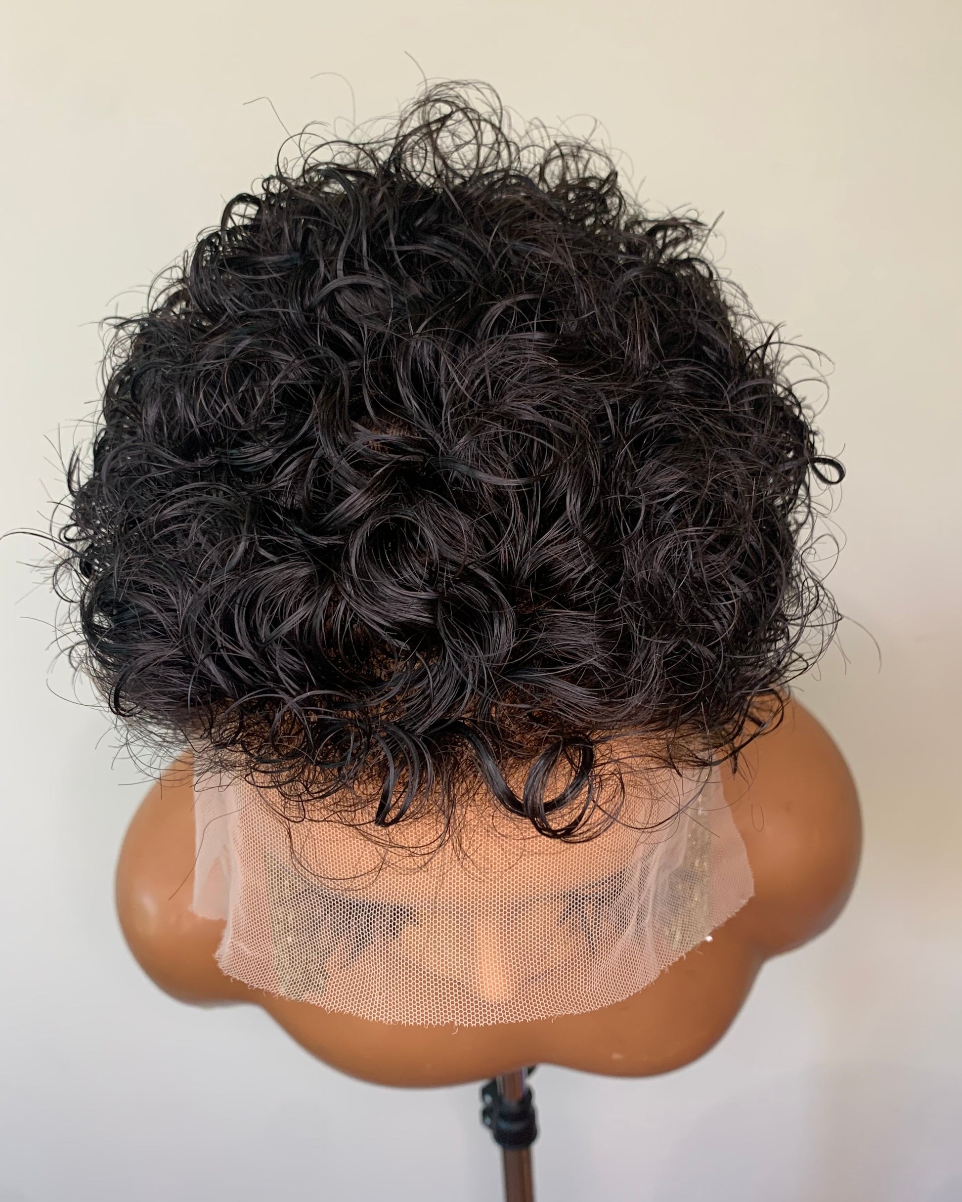 Black curly wig on a mannequin head against a white background